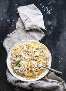 Pasta spaghetti with creamy mushroom sauce and basil in white ceramic plate over old grunge dark table