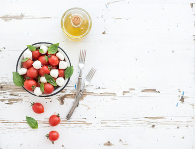 Caprese salad cherry tomatoes and mozzarella in metal bowl with olive oil on rustic white wooden backdrop  top view
