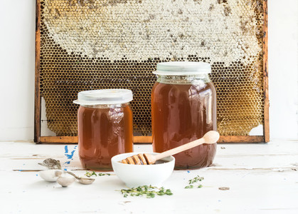 Jars of honey on white rustic wooden table with honeycombs at the backdrop