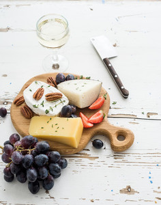 Cheese appetizer selection or wine snack set Variety of cheese grapes pecan nuts strawberry and honey on round wooden board over rustic white backdrop