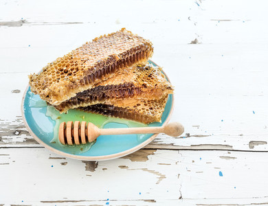 Honeycomb with honey dipper on blue ceramic plate over rustic white wooden table