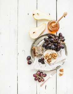 Camembert cheese with grape  walnuts  pear and honey on vintage metal plate over white rustic wood backdrop  top view