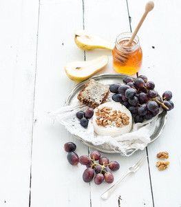 Camembert cheese with grape  walnuts  pear and honey on vintage metal plate over white rustic wood backdrop