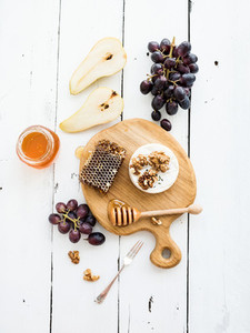 Camembert cheese with grape  walnuts  pear and honey on oak serving board over white rustic wood backdrop  top view