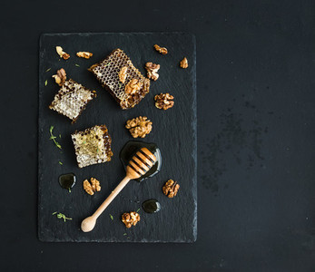 Honeycomb  walnuts and honey dipper on black slate tray over grunge dark backdrop  top view