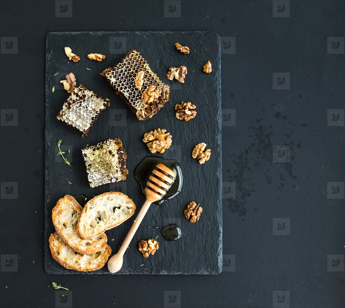 Honeycomb  walnuts  bread slices and honey dipper on black slate tray over grunge dark backdrop  top view