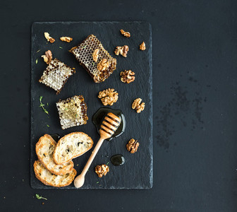 Honeycomb  walnuts  bread slices and honey dipper on black slate tray over grunge dark backdrop  top view