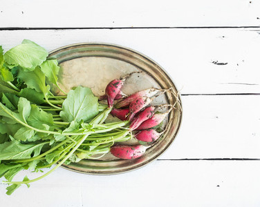 Bunch of fresh dirty garden radishes on vintage metal tray over rustic white wooden backdrop top view