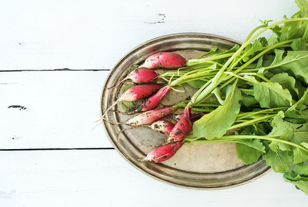 Bunch of fresh dirty garden radishes on vintage metal tray over rustic white wooden backdrop top view