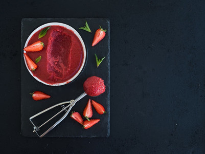 Strawberry sorbet or ice cream with fresh berries  mint and metal scooper on black slate tray over dark grunge backdrop  top view