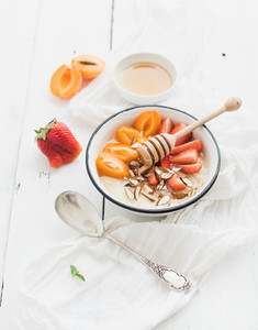 Healthy breakfast set  Rice cereal or porridge with fresh strawberry  apricots  almond and honey over white rustic wood backdrop  top view