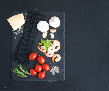 Ingredients for black pasta with seafood Shrimps spaghetti basil garlic spices parmesan cheese and  cherry tomatoes on dark grunge backdrop