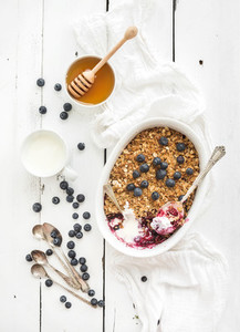 Healthy breakfast  Oat granola berry crumble with fresh blueberries  yogurt and honey in ceramic baking dish over white rustic backdrop