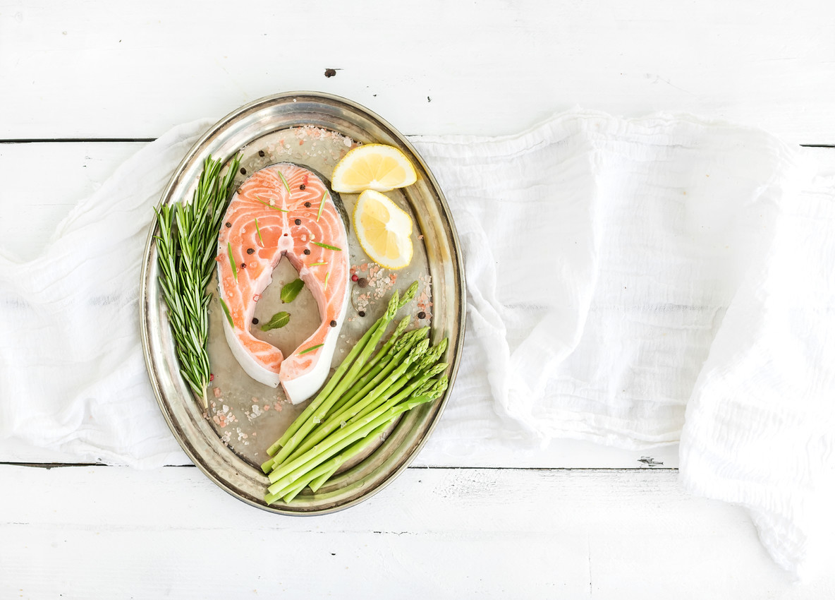 Raw salmon steak with asparagus  lemon  spices and rosemary on vintage silver tray over white wooden backdrop  top view