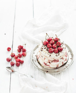 Pavlova cake with fresh cherry  cheese cream and chocolate chips in vintage silver plate over white rustic wooden background