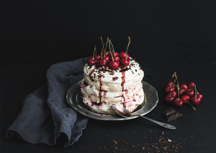 Pavlova cake with fresh cherry cheese cream and chocolate chips in vintage silver plate over dark grunge background