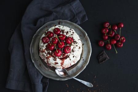 Pavlova cake with fresh cherry  cheese cream and chocolate chips in vintage silver plate over dark grunge background  top view