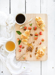 Freshly baked almond croissants with garden strawberries and honey on serving board over white rustic wood backdrop