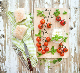 Ciabatta bread with banch of cherry tomatoes basil and mozzarella cheese on rustic wooden board over old white backdrop top view