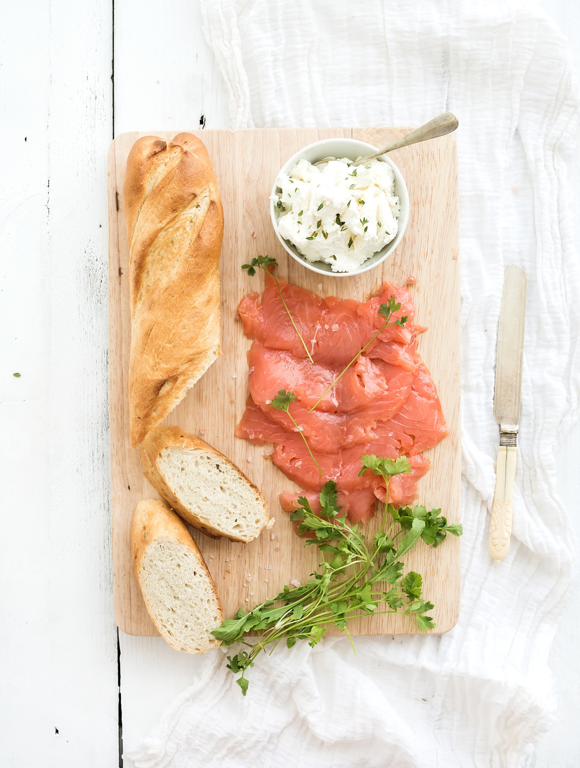 Salmon  ricotta and fresh parsley with baguette on a rustic wooden board over white wood background  Top view