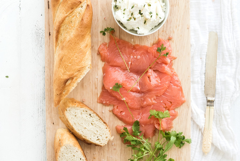 Salmon, ricotta and fresh parsley with baguette on a rustic wooden board over white wood background. Top view