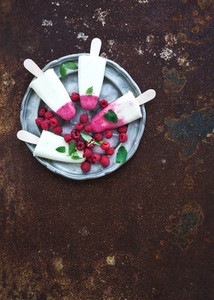 Raspberry lime yougurt ice creams or popsicles with fresh berries and ice cubeson vintage silver plate over grunge metal backdrop  top view