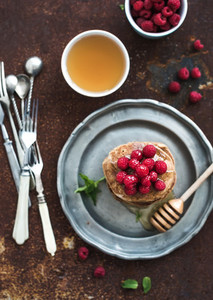 Breakfast set  Buckwheat pancakes with fresh raspberries  honey and mint leaves over grunge metal background  top view