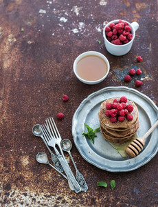 Breakfast set Buckwheat pancakes with fresh raspberries honey and mint leaves over grunge metal background