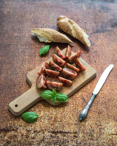 Ripe kumato tomatoes  basil leaves and knife on a rustic wooden chopping board over grunge rusty metal backdrop  top view