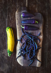 Violet chili peppers  beans and yellow zucchini on rustic wooden chopping board over dark wood background