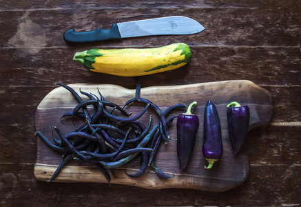 Violet chili peppers  beans and yellow zucchini on rustic wooden chopping board over dark wood background