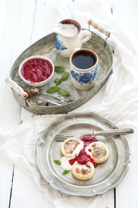 Breakfast set Russian cottage cheese pancakes or syrniki on a vintage metal plate with raspberry jam sour cream and coffee Rustic white backdrop