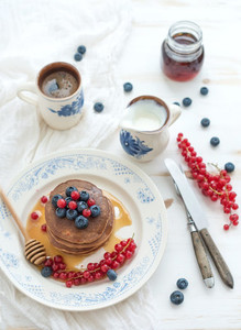 Breakfast set  Buckwheat pancakes with fresh berries  honey  sour cream and cup of coffee over white wooden background