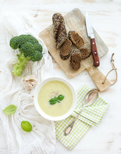 Broccoli cream soup with sunflower seeds  fresh basil and bread in bowl over white wooden table