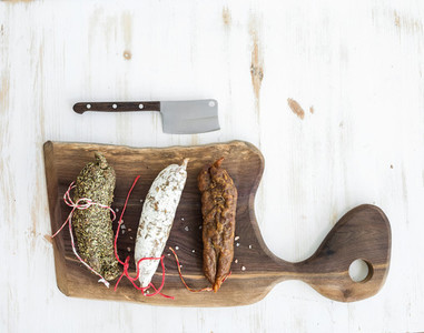 French alsacian smoked salamis on rustic walnut wooden chopping board over white backdrop top view