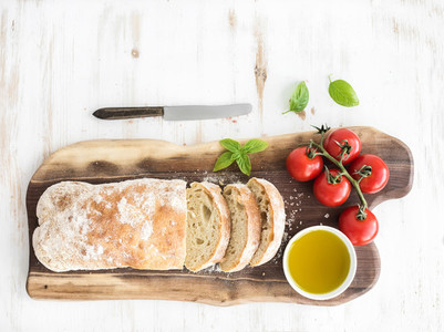 Freshly baked ciabatta bread with cherry tomatoes olive oil basil and salt on walnut wood board over white background top view