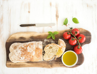 Freshly baked ciabatta bread with cherry tomatoes  olive oil  basil and salt on walnut wood board over white background  top view