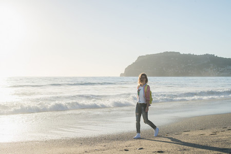 Young woman in red checkered shirt  jeans  white sneakers walking along beach and the stormy ocean on sunny winter day