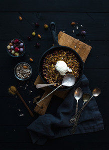 Healthy breakfast Oat granola crumble with frozen fresh berries  seeds and ice cream scoopin irom skillet pan on rustic wooden board over dark backdrop