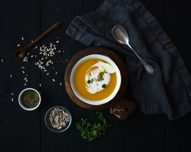 Pumpkin soup with cream seeds and spices in rustic metal bowl over black background Top view