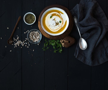 Pumpkin soup with cream seeds and spices in rustic metal bowl over black background Top view