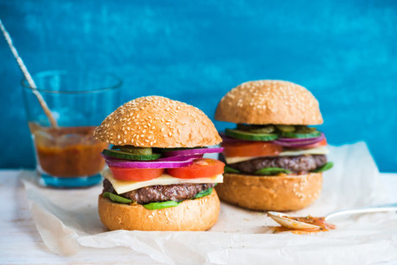 Fresh beef burger with cheese  vegetables and spicy tomato sauce on paper  blue wooden background