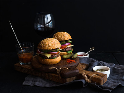 Fresh beef burgers on rustic wooden boards with glass of wine and tomato sauce  black background