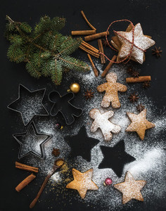 Cooked Christmas holiday traditional gingerbread cookies with sugar powder  anise and cinnamon sticks on black background