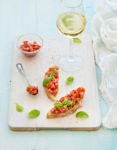Tomato and basil bruschetta sandwich on white wooden serving board over rustic blue background top view