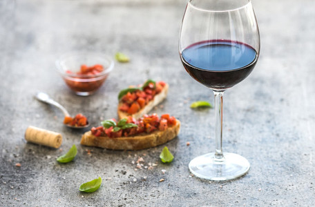 Wine appetizer set Glass of red wine brushettas with fresh tomato and basil on over rustic grunge grey surface