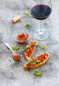 Wine appetizer set Glass of red wine brushettas with fresh tomato and basil on over rustic grunge grey surface