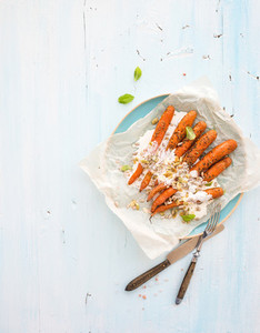 Roasted young carrots with cream and seeds in ceramic plate over blue wooden background