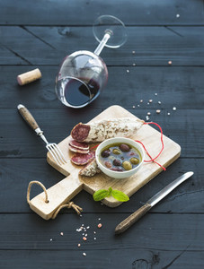 Wine appetizer set Glass of red wine French sausage and olives on black wooden backdrop