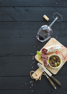 Wine appetizer set  Glass of red wine  French sausage and olives on black wooden backdrop